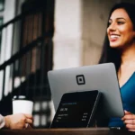 Businesswoman smiling while helping a customer with a digital payment on a tablet at an outdoor cafe.