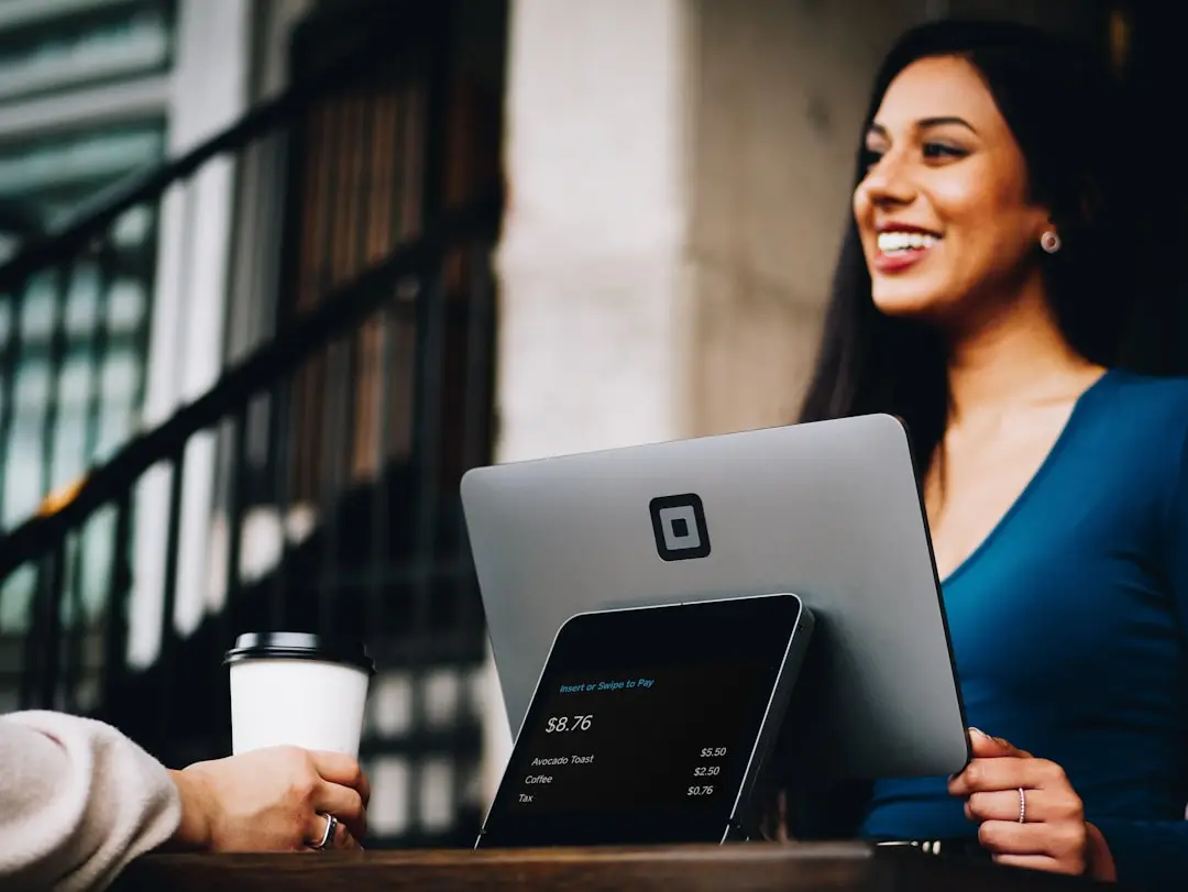 Businesswoman smiling while helping a customer with a digital payment on a tablet at an outdoor cafe.